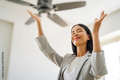Joyful Woman Relishing Cool Breeze Under Ceiling Fan in Modern Home.
