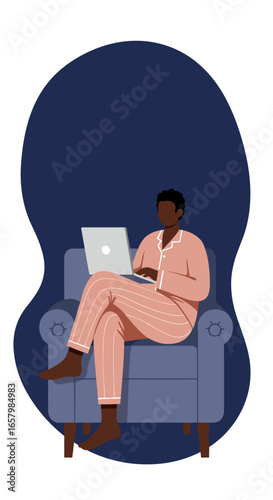 African American man in pajamas works on a laptop from home, sitting comfortably in an armchair. Ideal for remote work, relaxation, or online learning concepts.