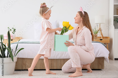 Cute little girl greeting her mom for Mother's Day with gift bag and yellow t...