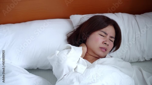 Asian woman suffering from neck pain after sleeping uncomfortable bad posture, female experiencing stiff ,sprain neck ,crick in the neck, muscle tension and discomfort in bed, unhealthy sleep position