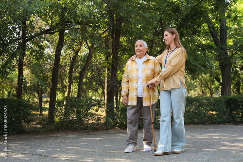 Senior woman with stick and caregiver walking in park