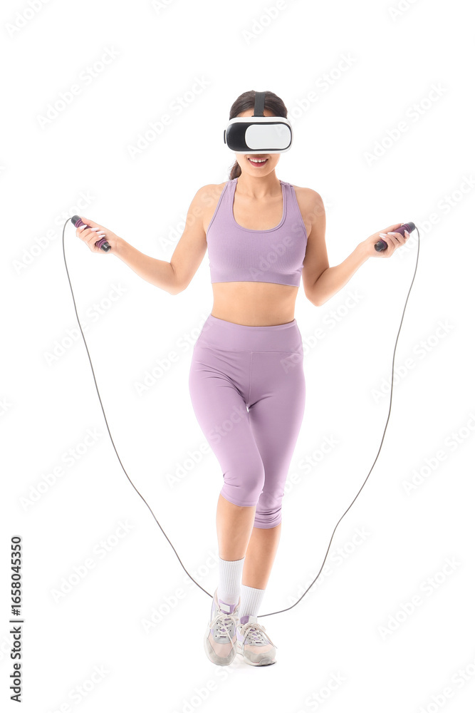 Obraz premium Sporty young woman in VR glasses exercising with skipping rope on white background