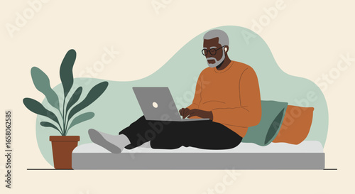 Senior Black man working comfortably on a laptop from home. Represents remote work, online education, or digital communication for older adults.