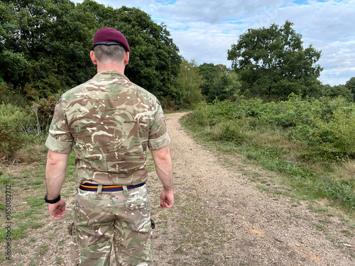 Close-up UK Army officer in maroon beret, REME stable belt, standing arms down, back to camera in woodland, British military personnel in field.