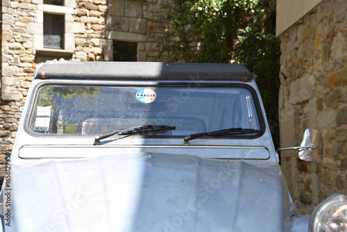 Closeup of vintage Citroën 2CV windshield and mirror parked by rustic stone wall, retro detail highlighting timeless French automotive design and nostalgic travel lifestyle.