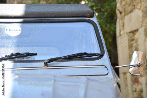 Closeup of vintage Citroën 2CV windshield and mirror parked by rustic stone wall, retro detail highlighting timeless French automotive design and nostalgic travel lifestyle.