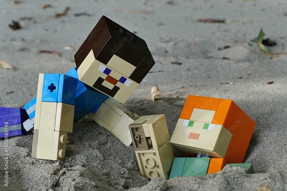 Fototapeta premium LEGO Mincecraft large action figures of Steve rescuing friend Alex stuck chest deep in sand on bank of Danube river, southern Slovakia.