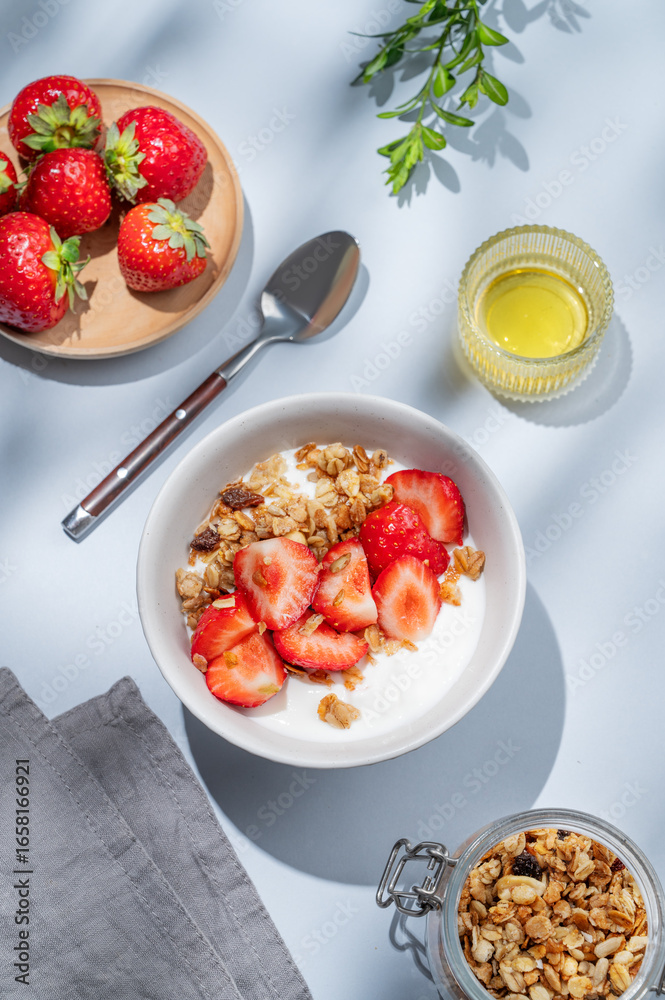 Granola or muesli with natural greek yogurt, strawberry and honey in a bowl on a blue background Granola or muesli with natural greek yogurt, strawberry and honey in a bowl on a blue background
