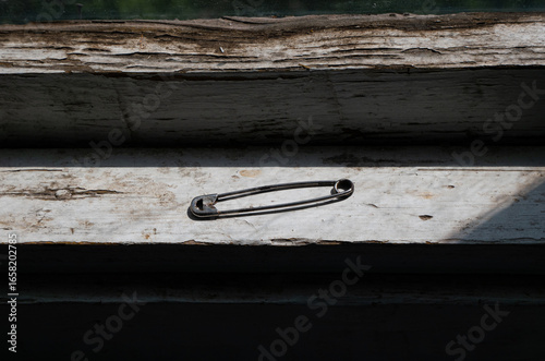 A Single Safety Pin Lying on a Weathered and Cracked Wooden Window Sill

