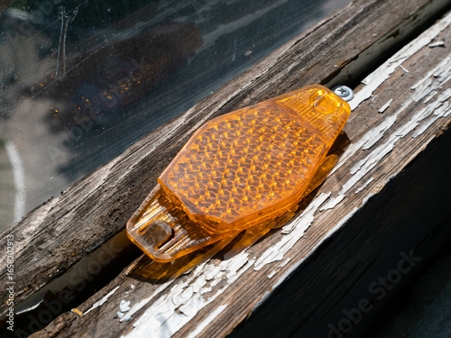 Orange Bicycle Reflector Lying on a Cracked and Peeling Window Frame