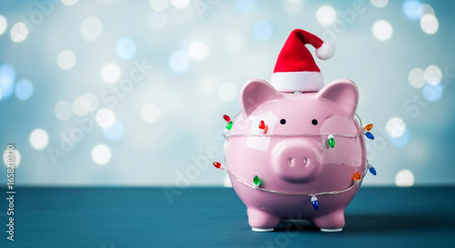 Saving for the holidays is shown with this cute pink piggy bank wearing a Santa hat and festive lights a perfect concept for a Christmas budget or holiday fund