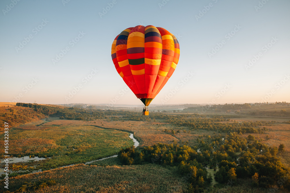 Naklejka premium Hot air balloon flying over green landscape at sunrise