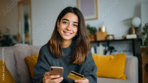 A woman is sitting on a couch with a cell phone and a credit card in her hands
