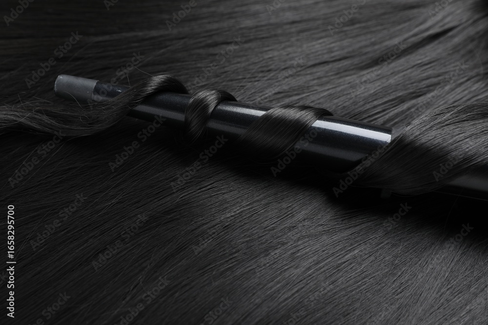 Naklejka premium Curling iron with shiny black hair, closeup