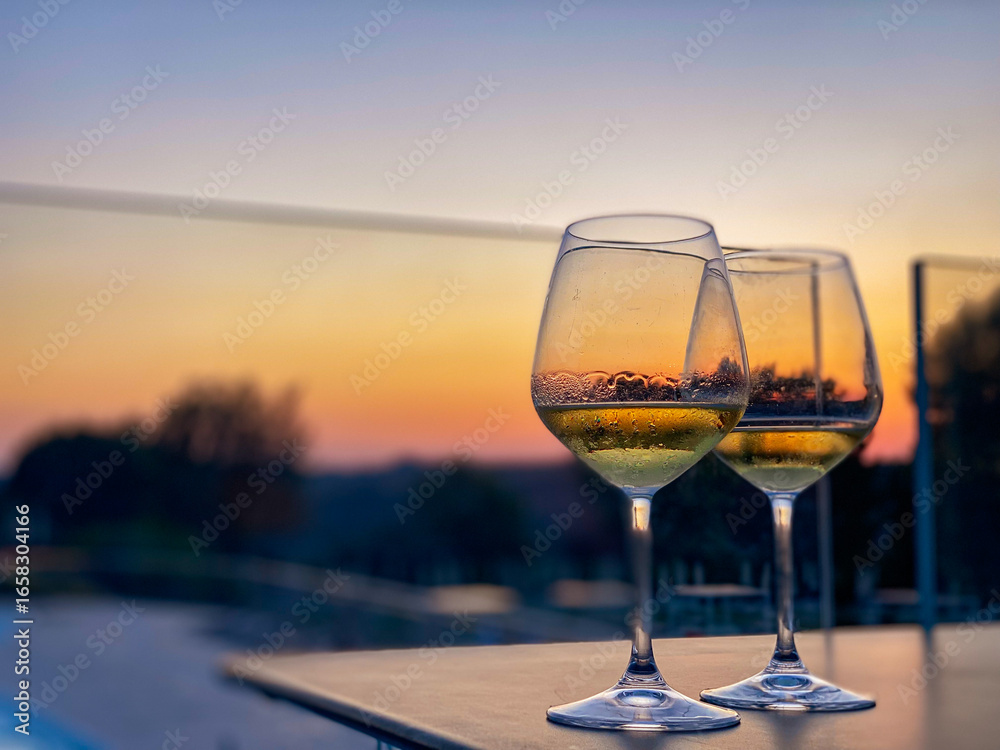 Obraz premium Sunset-lit wine glasses resting on rustic table, bathed in warm golden light of Tuscan landscape, evoking intimate evening ambiance