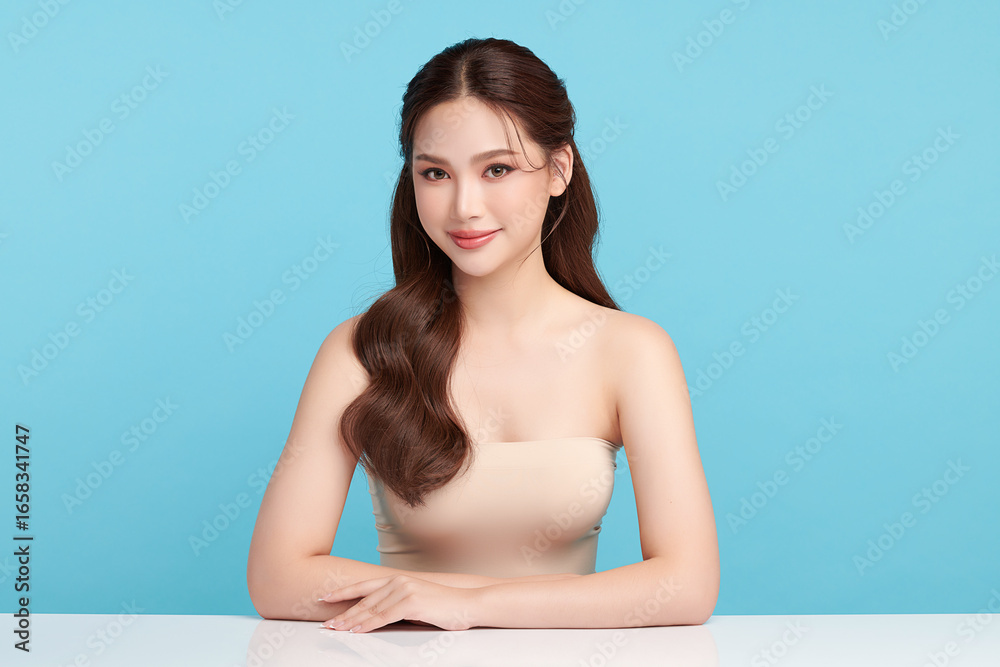 Obraz premium A beautiful young Asian woman with clean, fresh skin against a blue background. Skincare, facial treatment, cosmetology, beauty, and spa. An elegant portrait of an Asian woman.