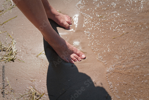 Canvas Print Bare feet wade through shallow, sunlit ocean water on sandy beach, water gently lapping at toes