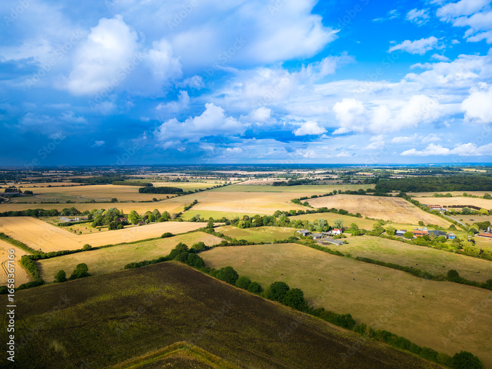 Obraz premium Early evening UAV view of agricultural land in the East of England, with a farm house near the centre of the image. Storm clouds can be seen gathering.