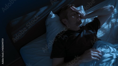 Young man unable to sleep, suffering from insomnia lies awake in bed at night. Sleep disorders, stress anxiety and overthinking. Depression and burnout. Space for text