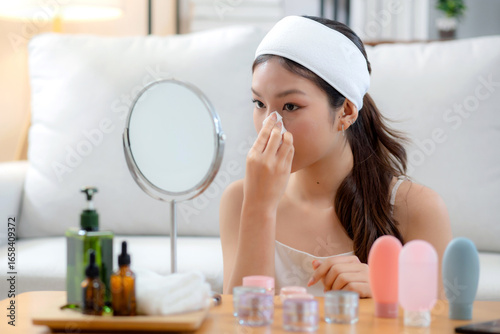 Beautiful young asian woman smile with skin care use oil blotting paper on face looking mirror in the room, beauty woman happy and clean makeup and cosmetic with tissue, skincare and health