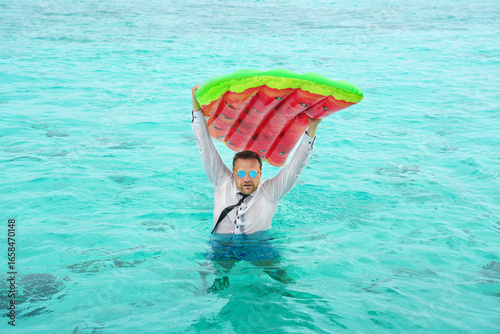  Business man with with colorful swimming mattress in tropical beach vacation. Announcement, save your vacation, off on vacation concept.