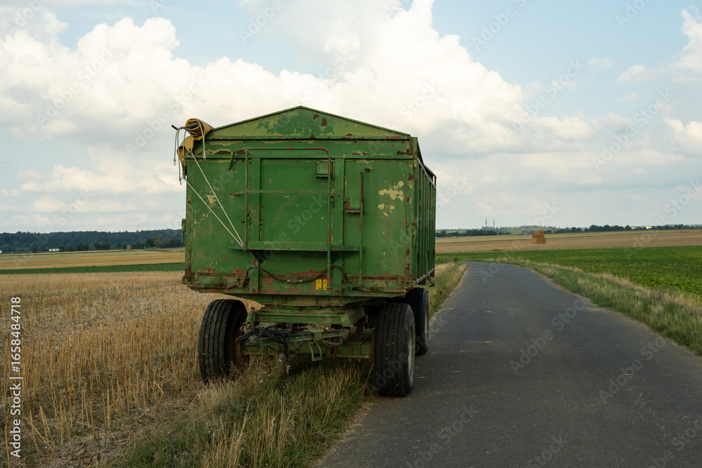 Obraz premium A farmer's large green dump trailer stands in a field. The picture shows the start of the harvest season.