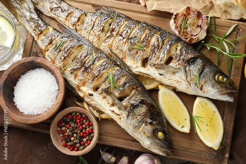 Принти на полотні Tasty roasted seabass fish served with rosemary and lemon on wooden table, flat lay