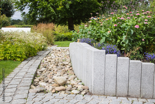 Modern Garden Design and Landscaping:Raised bed fenced by concrete blocks in different heights vertically erected-planted with flowers, perennial herbs-surrounded by grass, cobble and pebble stones