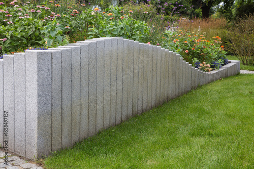 Modern Garden Design and Landscaping:Raised bed fenced by concrete blocks in different heights vertically erected-planted with flowers, perennial herbs-surrounded by grass, cobble and pebble stones