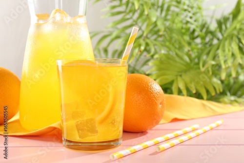 Refreshing soda water with orange slice in glass, jug and fresh fruits on pink wooden table, closeup