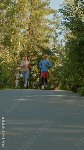 Wallpaper Mural Vertical low angle shot of young man and woman in warm sportswear jogging together in forest on chill summer day Torontodigital.ca