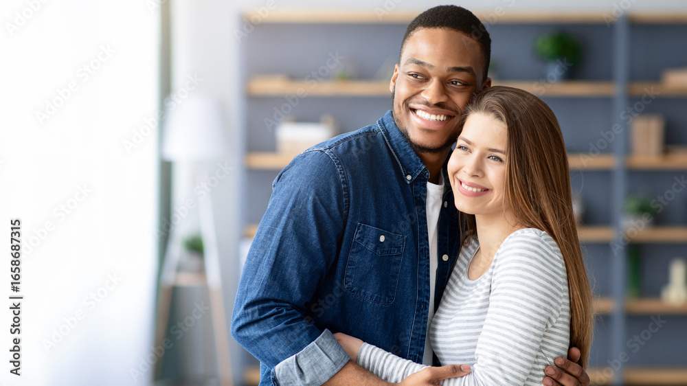 Fototapeta premium Portrait Of Young Loving Multiracial Couple Embracing At Home, Smiling Happy Millennial Black Man And White Woman Hugging In Living Room, Enjoying Spending Time Together, Copy Space