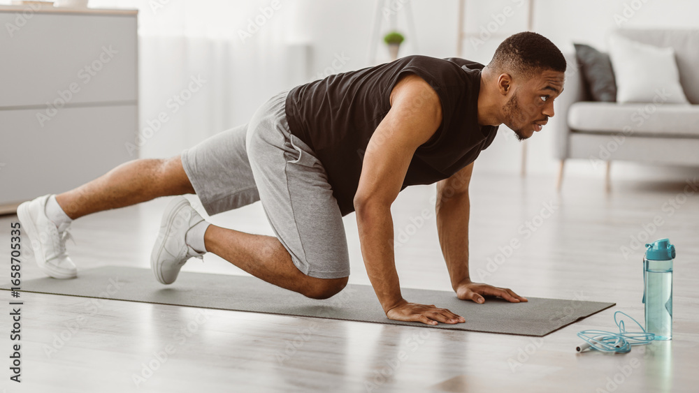 Fototapeta premium Sporty African American Man Doing Running Plank Exercise At Home. Side View Of Athletic Guy Training In Living Room. Male Fitness Workout And Bodybuilding. Sport Motivation Concept. Panorama