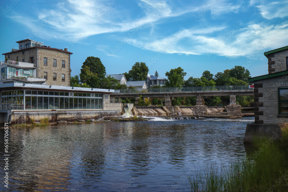 Naklejka premium Small hydroelectric power station along river rapids and waterfall, footbridge, daytime, sunny, nobody
