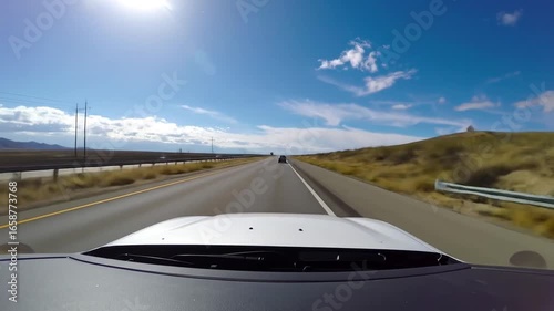 Driving view on a bright day, asphalt highway stretching to distant mountains under a blue sky with fluffy clouds