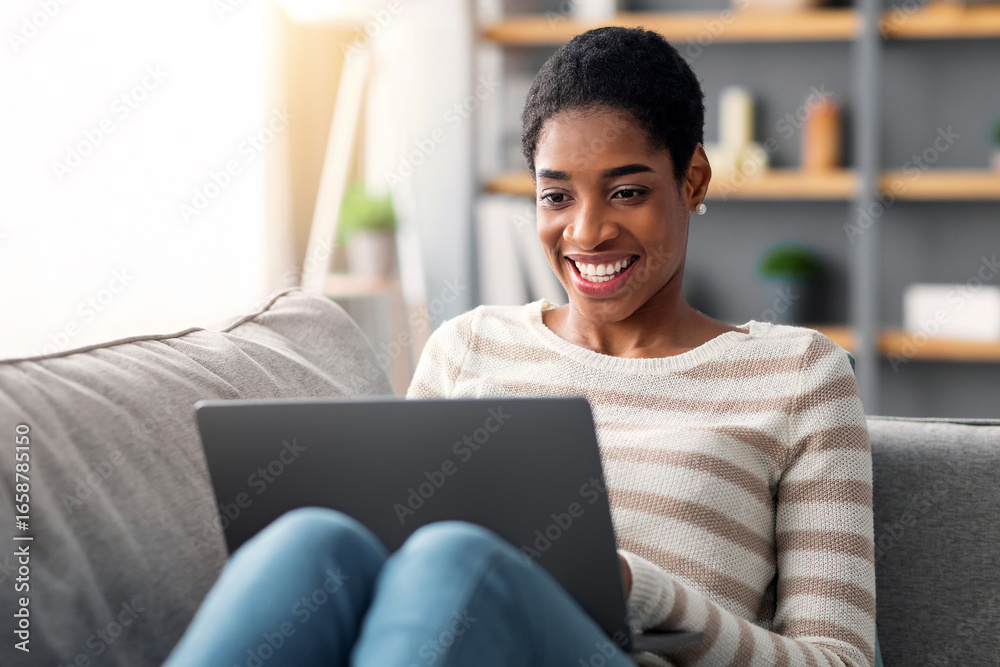Naklejka premium Happy Black Female Browsing Internet On Laptop While Relaxing At Home, Cheerful Young African American Woman Resting On Couch In Living Room, Checking New Website For Online Shopping, Closeup