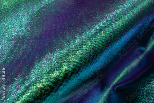 Abstract close-up of shimmering iridescent fabric in green, blue and violet hues with metallic shine, creating a glossy surface ideal for fashion, luxury, design, art and creative concepts.