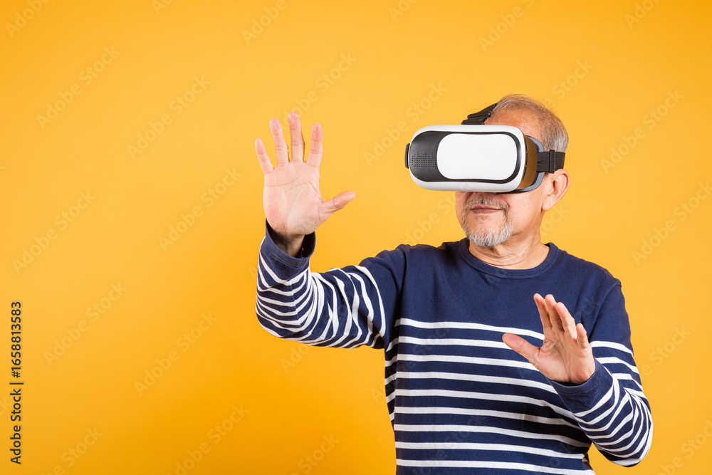 Portrait Asian smiling old man touching at something in a virtual reality glasses headset studio shot isolated yellow background, Excited happy senior man pensioner using VR play simulation game Portrait Asian smiling old man touching at something in a virtual reality glasses headset studio shot isolated yellow background, Excited happy senior man pensioner using VR play simulation game