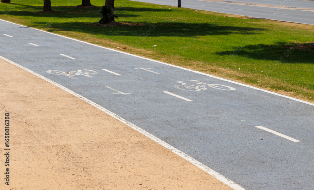 Obraz premium Bicycle path marked with lane lines for cyclists running parallel to a grassy area, providing a safe space for biking and outdoor activities in sunny weather.