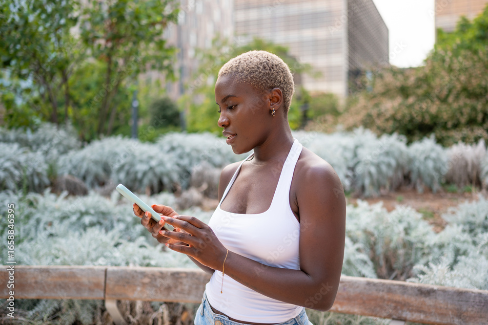 Fototapeta premium Young woman using smartphone in urban park setting