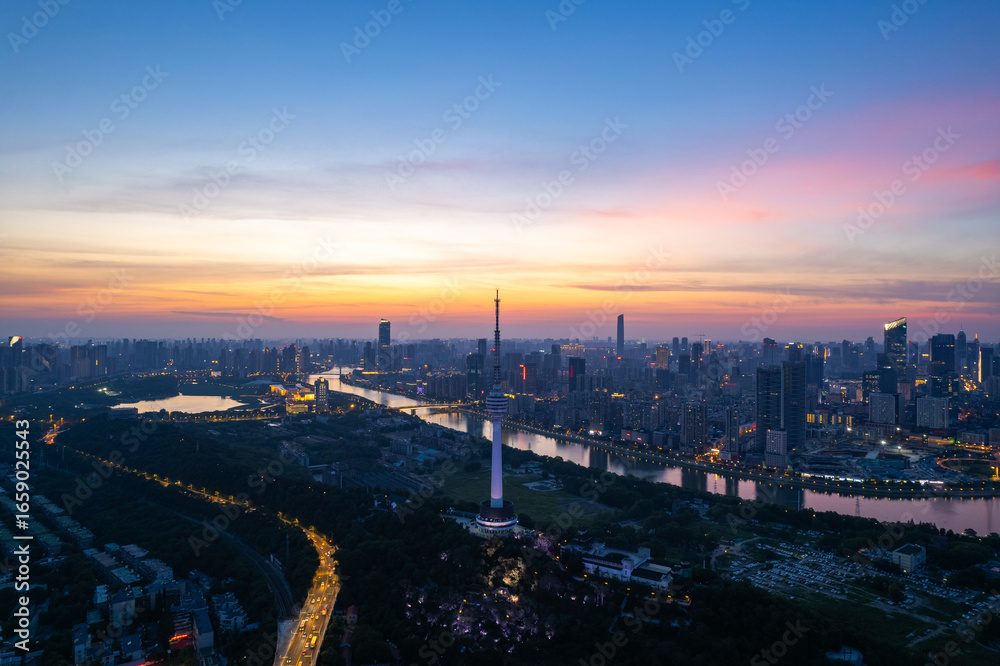 Naklejka premium Wuhan city skyline at dusk shows the river and bright lights illuminating the urban landscape.