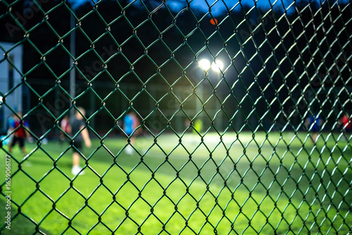 Wallpaper Mural People playing soccer behind a metal chain link fence at night Torontodigital.ca
