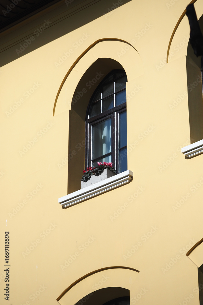 Obraz premium Decorative window with flowers on a yellow building facade
