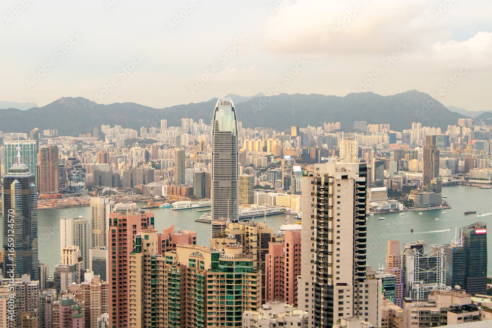 Fototapeta premium Landscape of scenery aerial view on top of buildings in town Hong Kong. City with white cloudy by bright sunlight in evening with hotels and office towers with orange sunlight in evening is background