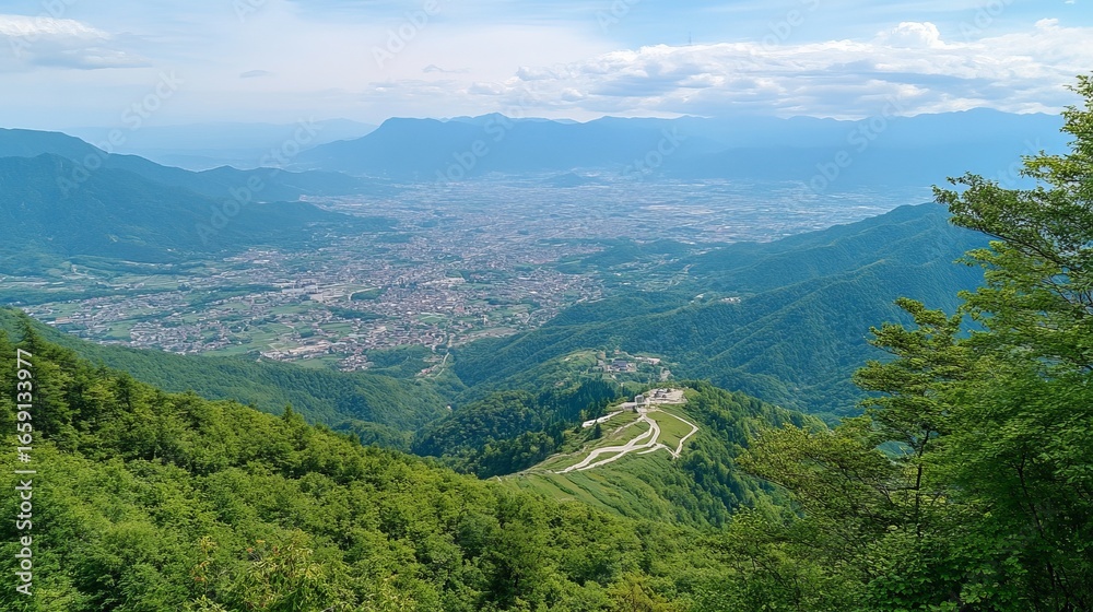 Fototapeta premium High-angle view of a valley, city, and mountains. Lush green hills surround a valley with a city nestled within. Mountain roads are visible