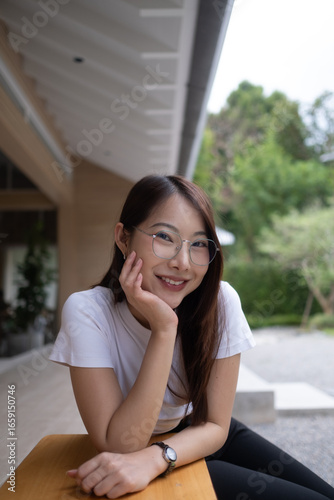 A woman wearing glasses and a white shirt is sitting on a wooden table. Cafe chilling time relax. Free Download A woman wearing glasses and a white shirt is sitting on a wooden table. Cafe chilling time relax. - GFXLoad
