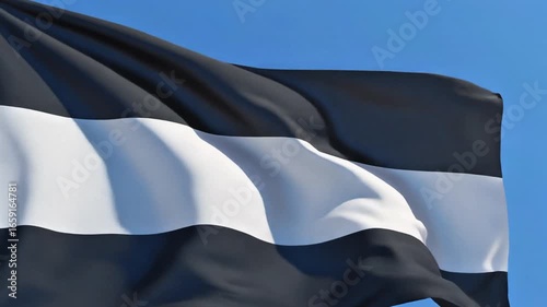 A black and white striped flag waves against a clear blue sky, the fabric rippling in the wind.