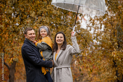 Family mother, father, daughter, beautiful happy together in autumn in nature with an umbrella under a leaf fall