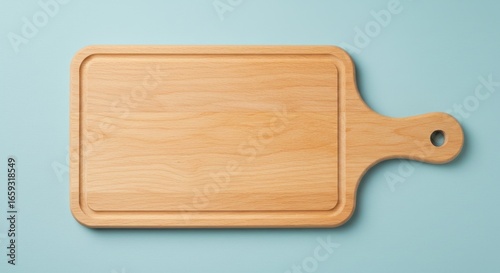 Top-down shot of a rectangular, light-colored wooden cutting board with a handle and a groove around the perimeter, against a blue background
