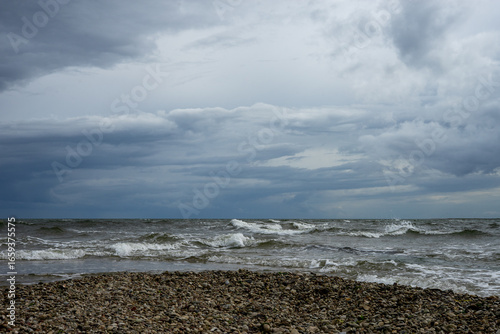 Fototapeta Naklejka Na Ścianę i Meble -  Pebble beach and Baltic Sea waves under a moody overcast sky.